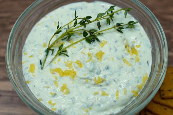 glass bowl of goat cheese spread garnished with fresh thyme sprigs and lemon zest