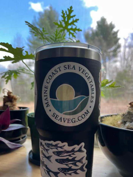 Tumbler with Maine Coast Sea Vegetables sticker on a table with plants in the background