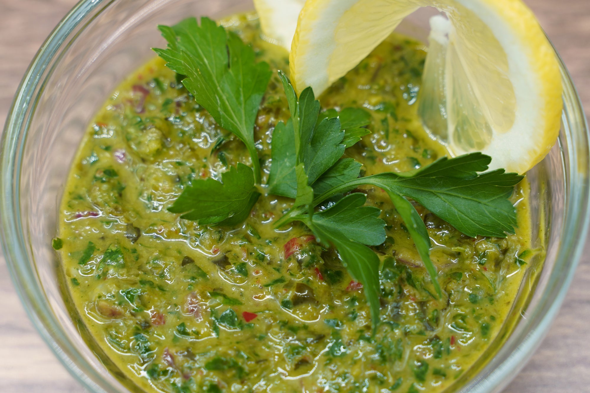 glass bowl of green chimichurri sauce garnished with whole leaf parsley and a lemon slice