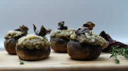 close-up of mushroom caps with suffing and topped with shredded cheese and a piece of red dulse seaweed on a wood cutting board