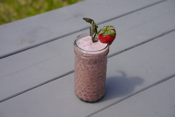 pink berry smoothie in a quilted mason jar on a gray picninc table with a trawberry on the rim and a frond of alaria sticking out
