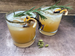 two rocks glasses with frothy grapefruit cocktails filled with ice and garnishde with a spiral of grapefruit rind, a piece of lacer, and a sprig of rosemary. The glass is rimmed with a mixture of brown kelp powder and sugar