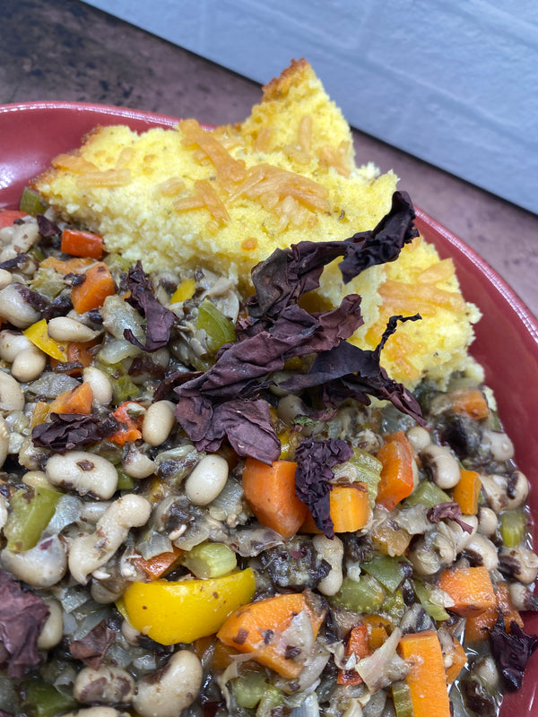 close up black-eyed peas, carrots, yellow peppers, and celery stew with grits topped with toasty cheese and a leaf of purple dulse seawweed