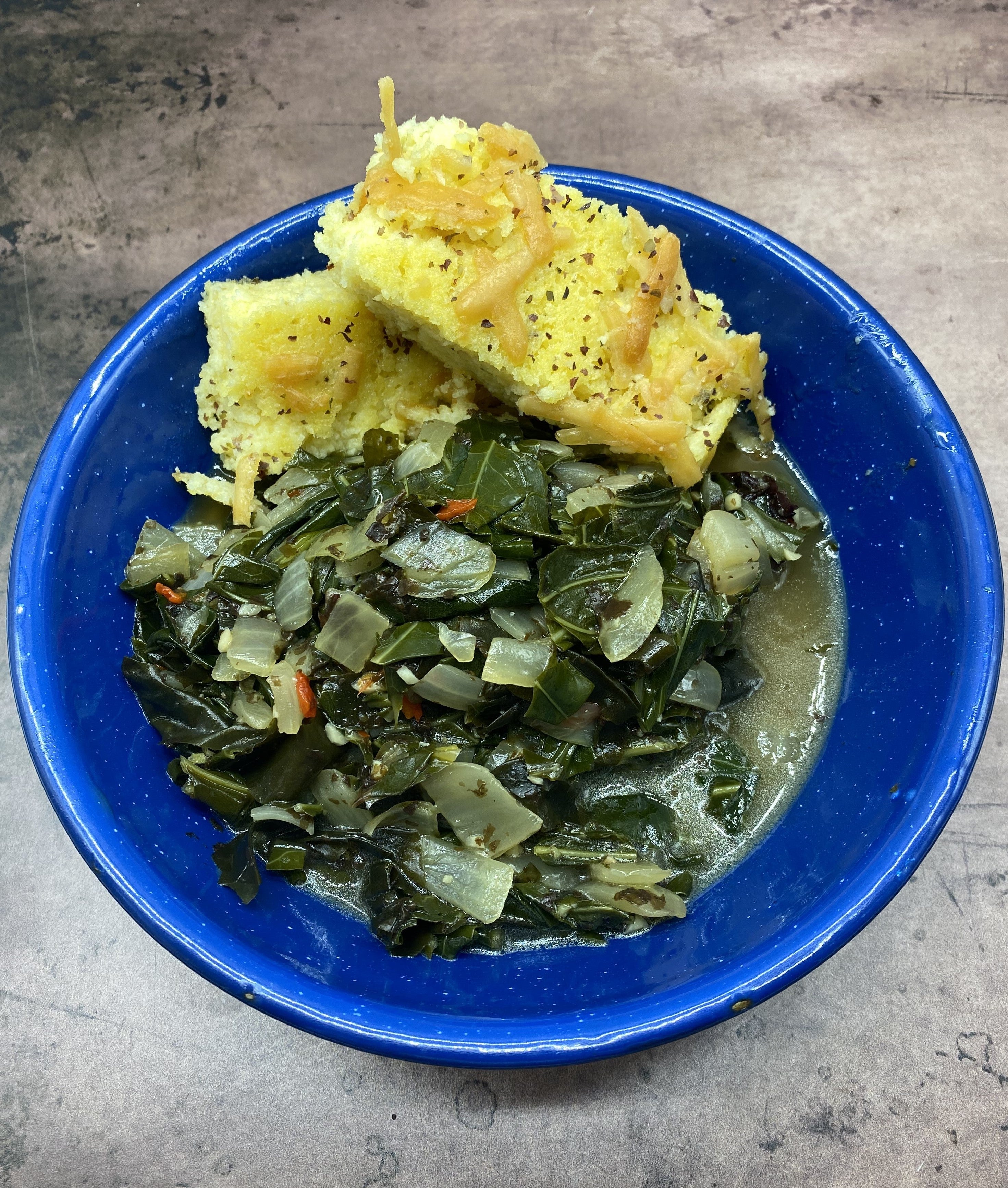 Blue enamelware bowl full of braised greend nad chopped spicy red pepper and onions with a side of cheese-topped grits