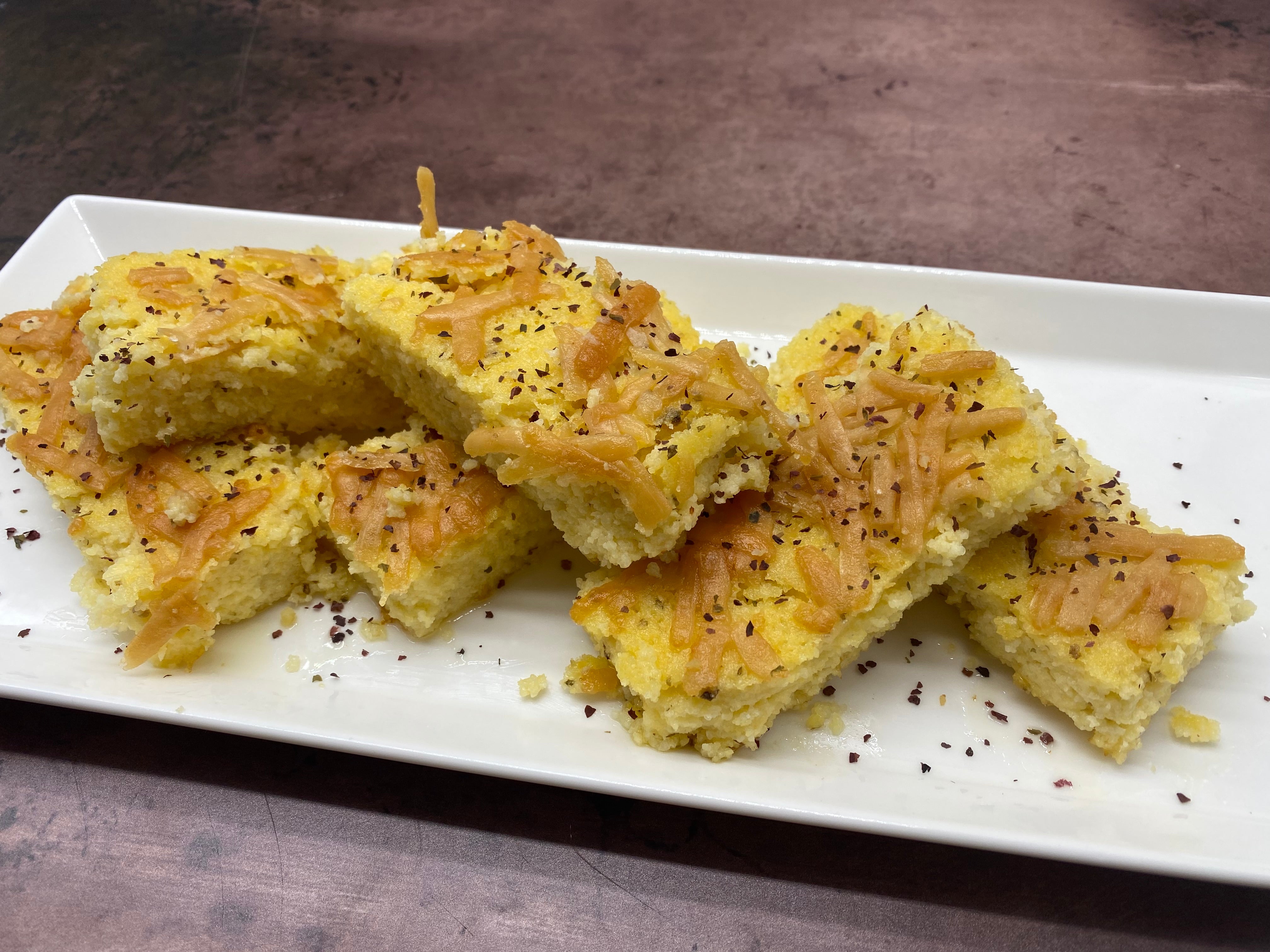 white rectangular plate with six peices of yellow grits cut in 1" by 3" rectangles and stacked overlapping slightly. Srinlkled with Triple Blend Seaweed Seasoning