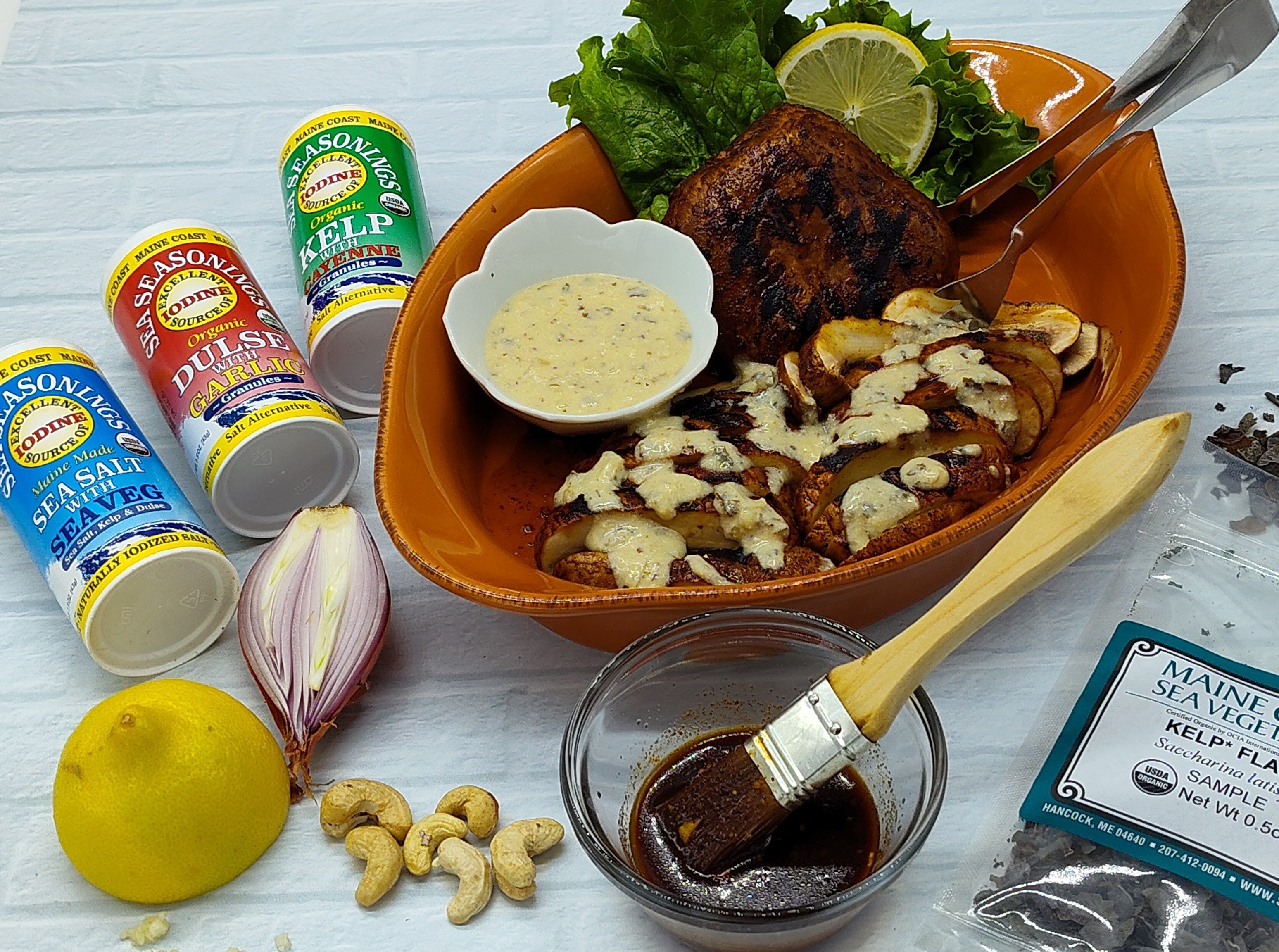 sea seasoning shakers on left with red plate of grilled mushrrom cap drizzled with creamy sauce and a basting bowl and brush in the foreground